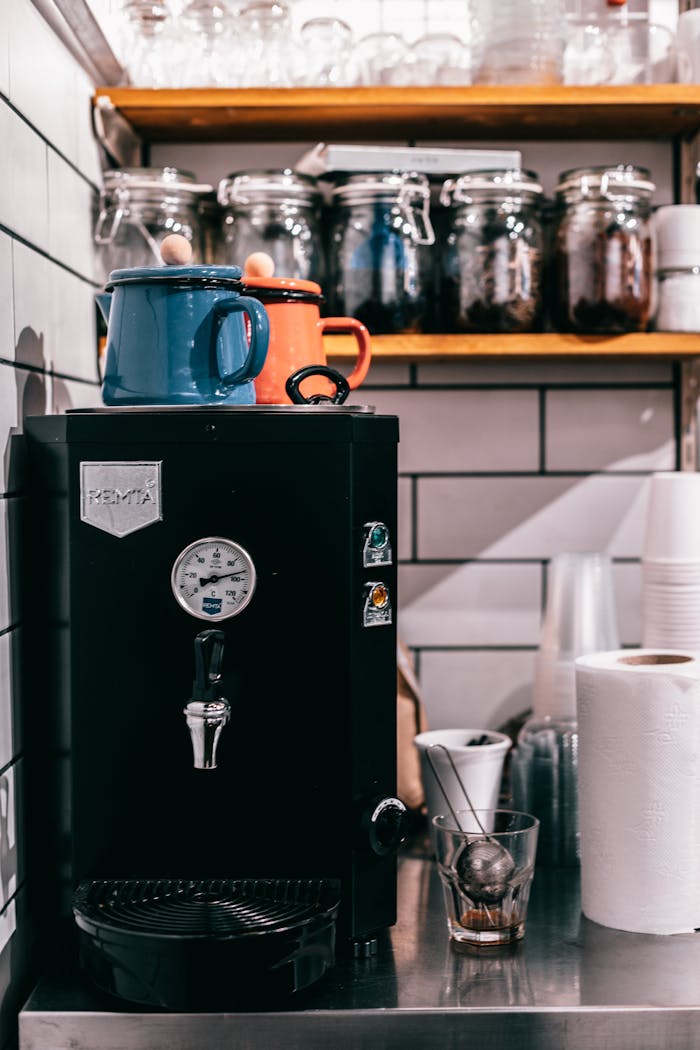 contact-img Black modern electric tea kettle with teapots on top placed on table with dishware in kitchen with jars on shelves